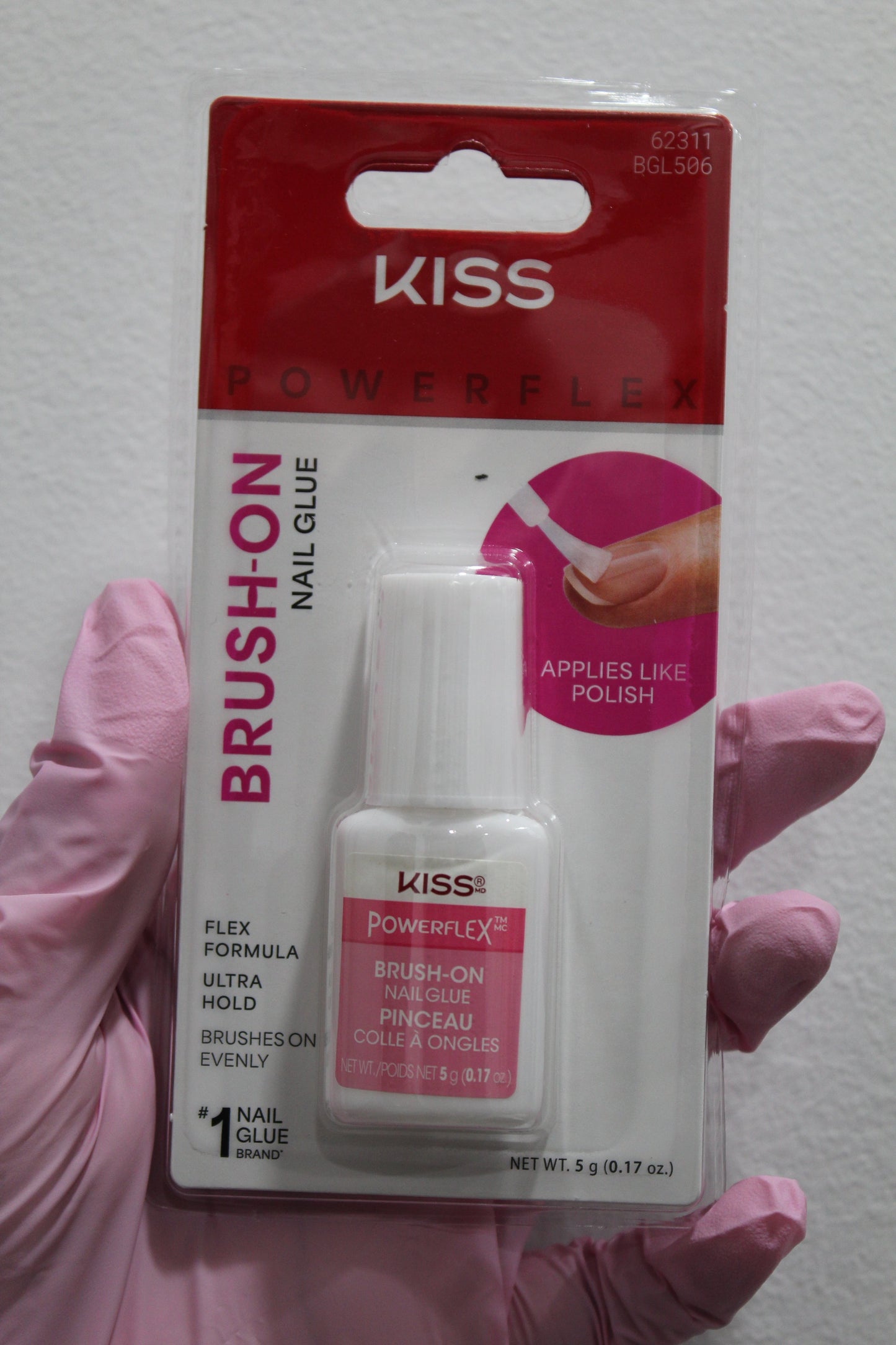 Kiss Brush-On Nail Glue packaging held by a gloved hand on a white background