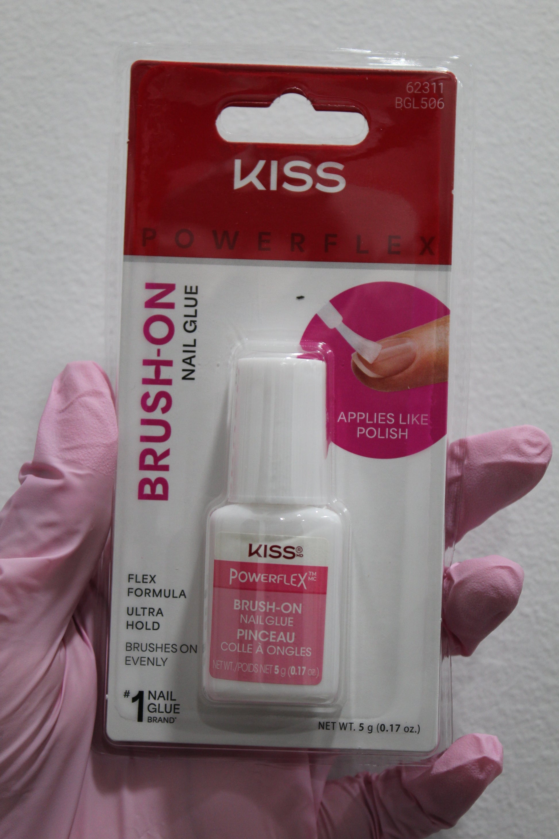 Kiss Brush-On Nail Glue packaging held by a gloved hand on a white background